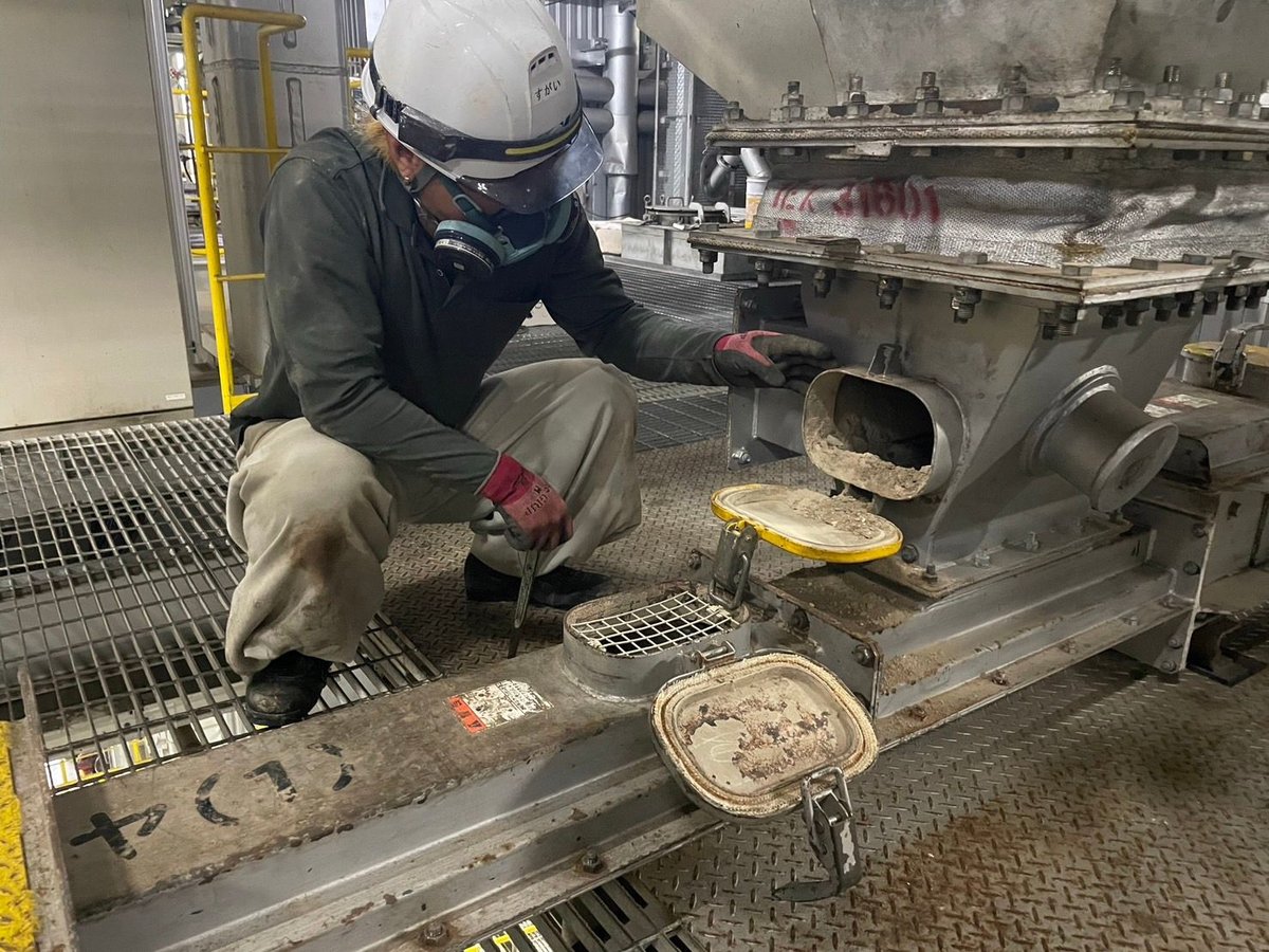 ホッパーの点検口を呼吸用保護具を着けて確認する作業員